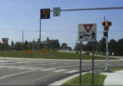 Yield here to pedestrians sign at a crosswalk with a flashing beacon