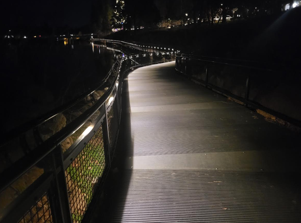 A curving path at night, lit only by a low strip of light along the handrail. 