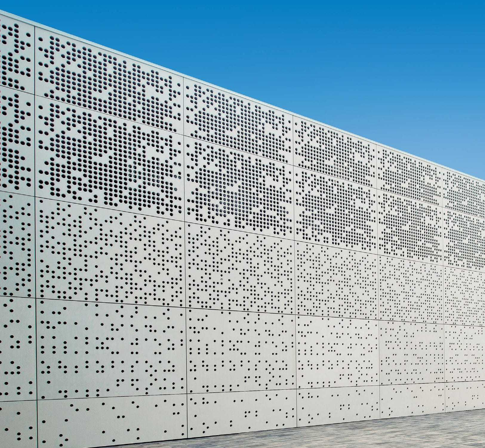 White perforated metal wall where the holes vary in size to create a wavy pattern.